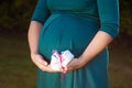 Small shoes for the unborn baby in the belly of pregnant woman. Pregnant woman holding small baby shoes relaxing at home in Royalty Free Stock Photo
