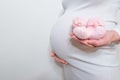 Small shoes for the unborn baby in the belly of pregnant woman. Pregnant woman holding small baby shoes relaxing at home in Royalty Free Stock Photo