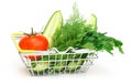 A small shopping basket with herbs, cucumber, tomato, parsley next to a fresh potted green salad on a white background