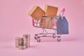 Small shopping cart with blank price tag and coins on a pink background. Shop trolley full of parcels Royalty Free Stock Photo