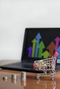 Small shopping cart full of coins on the table with stacks of coins and a laptop on it Royalty Free Stock Photo