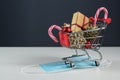 Small shopping cart with gift, christmas decoration and sweets on a surgical face mask against covid-19 infection, safe holiday Royalty Free Stock Photo