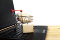 A small shopping cart with miniature shipping boxes stands on a laptop against a white background. Online shopping concept Royalty Free Stock Photo