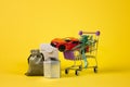 Small shopping trolley in a supermarket with purchases and gifts on a uniform yellow background Royalty Free Stock Photo