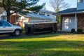 A small short beat up black and white dumpster containing wood debris located in a driveway in front of a garage door