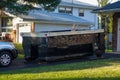 A small short beat up black and white dumpster containing wood debris located in a driveway in front of a garage door