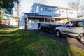 A small short beat up black and white dumpster containing wood debris located in a driveway in front of a garage door