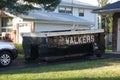 A small short beat up black and white dumpster containing wood debris seen in a driveway in front of a garage door