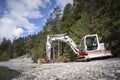 Small shovel digger standing on gravel next to lake and forest Royalty Free Stock Photo