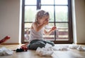 Small sick boy with cold at home sitting on ground, sneezing.