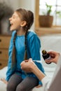 Small sick mischievous girl loudly refusing to take throat syrup