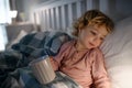 Small sick toddler girl lying in bed indoors at home, holding cup.