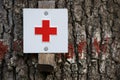 Small sign with a red cross on white background fixed to a tree