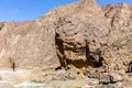 Small silhouette of a man walking next to big limestone rock in dry riverbed in Wadi Shawka, UAE.