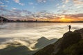 Small silhouette of tourist with backpack on rocky mountain slope with raised hands at sunrise on background of valley or river Royalty Free Stock Photo