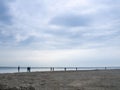 Small silhouettes of people on the shore. People in the distance stand and look at the sea. Overcast weather Royalty Free Stock Photo