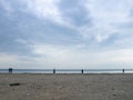 Small silhouettes of people on the shore. People in the distance stand and look at the sea. Overcast weather. Out of season at the Royalty Free Stock Photo