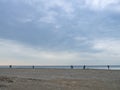 Small silhouettes of people on the shore. People in the distance stand and look at the sea. Overcast weather. Out of season at the Royalty Free Stock Photo