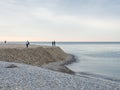 Small silhouettes of people on the shore. People in the distance stand and look at the sea. Overcast weather. Out of season at the Royalty Free Stock Photo