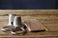 SMALL SILVER COLORED SCISSORS AND TWO METAL THIMBLES WITH DARNING WOOL ON A PIECE OF CARDBOARD