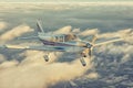 Small single engine airplane flying in the gorgeous sunset sky through the sea of clouds above the spectacular mountains