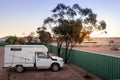 Small sized 4wd campervan parked on a camping site in the middle of the desert. Sunset time. Green fence and tree next to the car Royalty Free Stock Photo