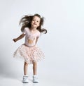 Small smiling cute girl in casual summer dress and sneakers jumping over white wall background Royalty Free Stock Photo