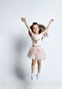 Small smiling cute girl in casual summer dress and sneakers jumping over white wall background Royalty Free Stock Photo