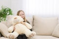 Small smiling girl sitting on the sofa with her toy teddy bear photo. Royalty Free Stock Photo