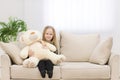 Small smiling girl sitting on the sofa with her toy teddy bear photo. Royalty Free Stock Photo