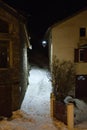 Small snowy path, between two mountain houses, at night lit by a lantern