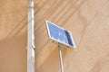 A small solar panel mounted on a metal pole is positioned next to a yellow building wall Royalty Free Stock Photo