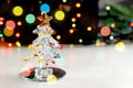 A small souvenir Christmas tree made of glass on the background of twinkling Christmas lights, bokeh effect.