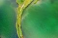 A small spit with a path covered with green grass on both sides, on a clear lake. Aerial photography