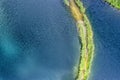 A small spit with a path covered with green grass on both sides, on a clear lake. Aerial photography