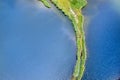 A small spit with a path covered with green grass on both sides, on a clear lake. Aerial photography