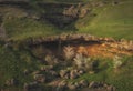 A small spring waterfall falls from a green hill into wild trees