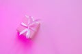 Small square gift in pink wrapping paper with ribbon on pink background, neon lighting.