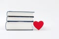 A small stack of books on a white background and a small red heart.