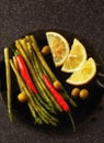 Small still life. on a black plate, a bunch of asparagus, red pepper and lemon wedges