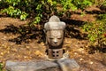 A small stone buddha statue in a Japanese garden surrounded by brown fallen pine needles and lush green trees and plants Royalty Free Stock Photo