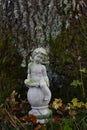 A small stone cherub statue sits at the base of a moss-covered tree Royalty Free Stock Photo