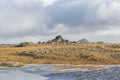 A small stony mountain sumit cairn with majestic mountain summit the background and small pond in the foreground under a stormy