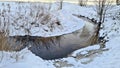 Small stream flows through forest with banks covered in snow and overgrown with reeds Royalty Free Stock Photo