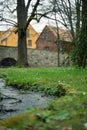 A small stream flows through a park, with a bridge and houses in the background Royalty Free Stock Photo