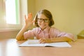 Small student in glasses sits at a desk with a notebook raised her hand showing 5 fingers. School, education, knowledge and childr Royalty Free Stock Photo