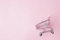 Small supermarket grocery push cart for shopping toy with wheels and pink plastic elements on pink pastel color paper flat lay Royalty Free Stock Photo
