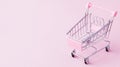 Small supermarket grocery push cart for shopping toy with wheels and pink plastic elements on pink pastel color paper flat lay Royalty Free Stock Photo