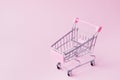 Small supermarket grocery push cart for shopping toy with wheels and pink plastic elements on pink pastel color paper flat lay Royalty Free Stock Photo