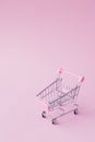 Small supermarket grocery push cart for shopping toy with wheels and pink plastic elements on pink pastel color paper flat lay Royalty Free Stock Photo